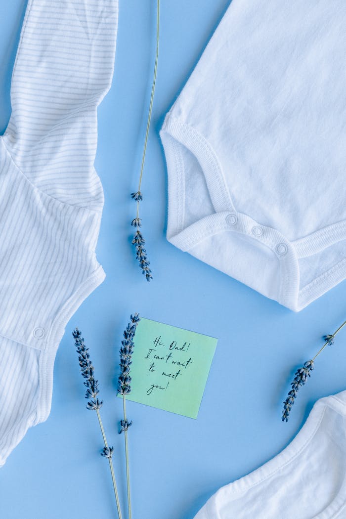 Flat lay of baby onesies with lavender and a note on blue background.