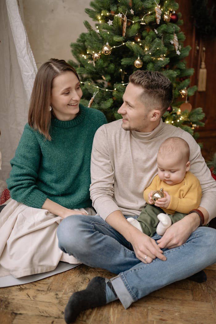 Smiling family of three enjoying Christmas together by the decorated tree.