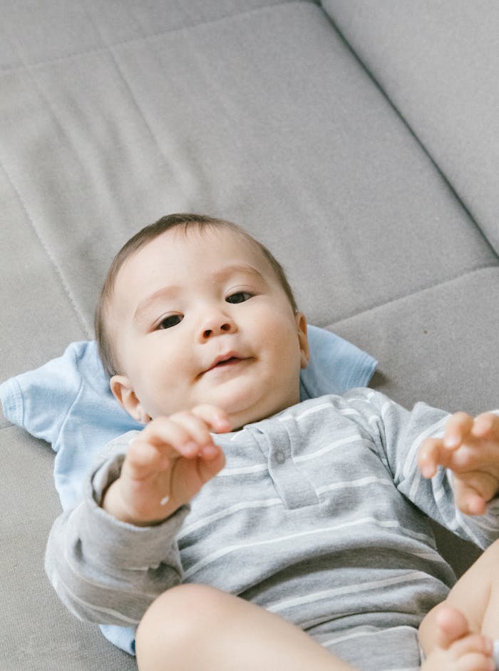 Cute baby lying on a couch, dressed in a striped onesie, captured from above.